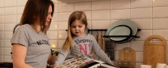 A mother and daughter enjoy reading a cookbook in a modern kitchen, sharing fun and learning together.