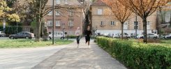A couple jogging together in an urban park surrounded by greenery and houses.