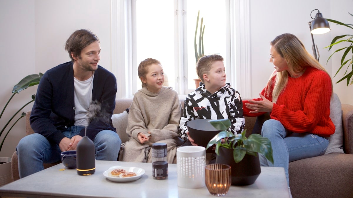 A family of four converse in a living room while a black volant diffuser is on the table.