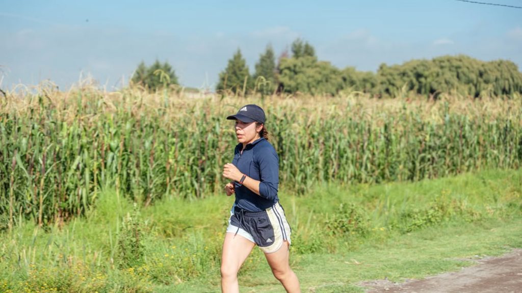 Woman jogging along a rural path next to a cornfield, enjoying fitness in nature.